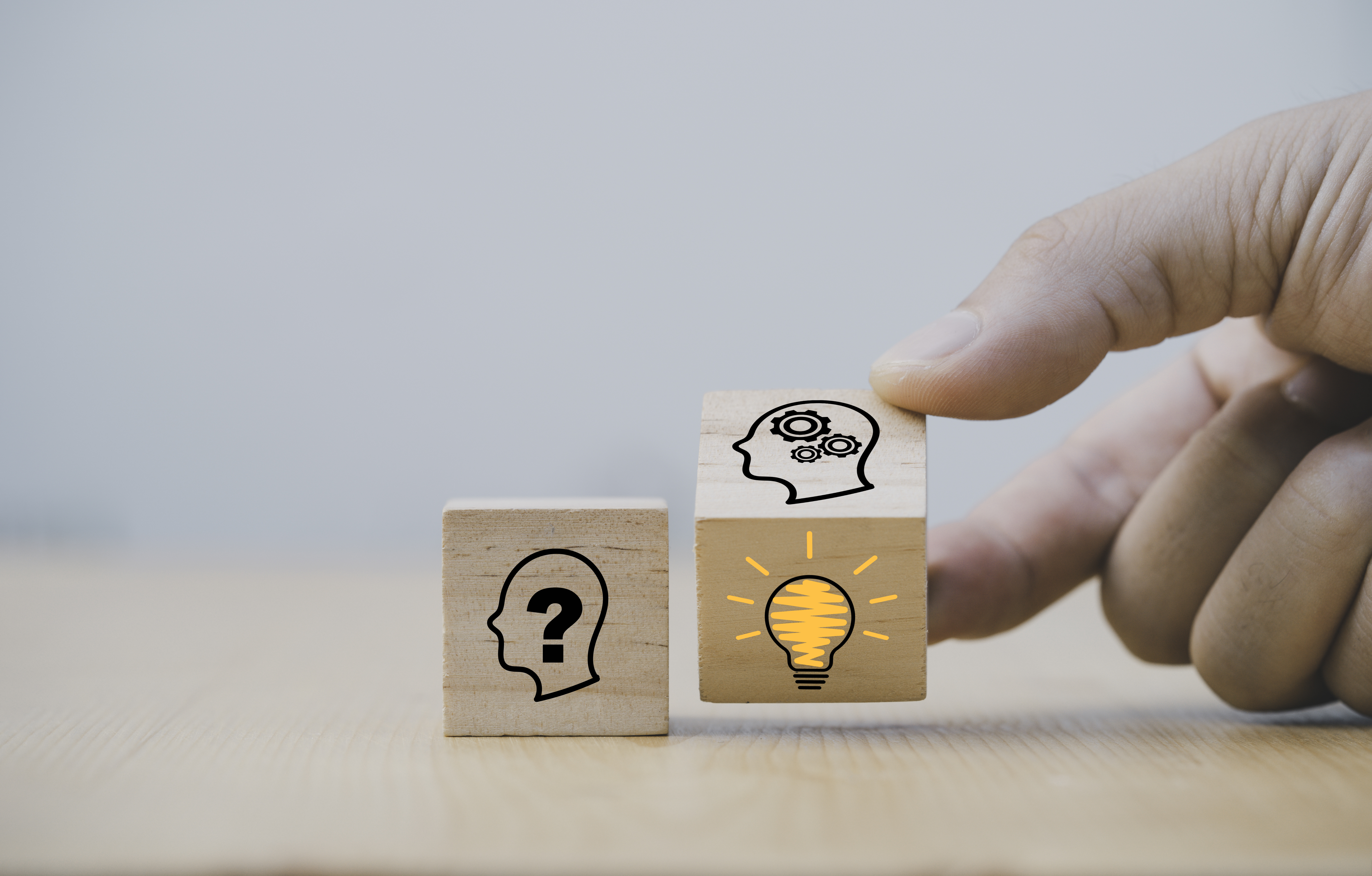 Eine Hand dreht einen Holzwürfel um und wechselt von dem Symbol eines denkenden Kopfes zu einer Glühbirne. So soll wiedergespiegelt werden wie aus einer kreativen Idee eine Innovation wird.  